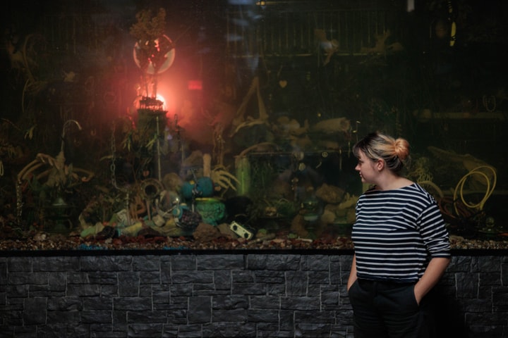 A woman wearing a striped shirt looks at an art installation behind her.