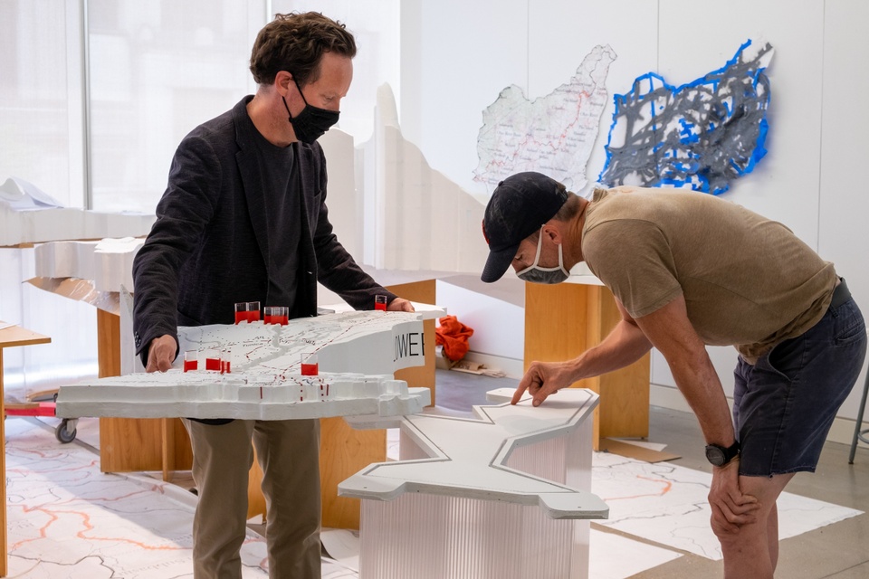 Two people inspect a platform built to hold a white topographic landscape model.