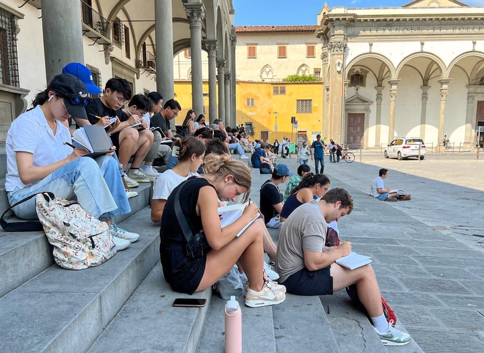 Students sit on the steps of a colonnade and sketch a plaza in Florence, Italy.