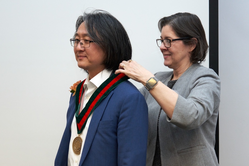 Woman bestows medallion on man.
