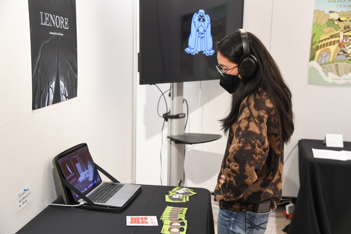 A student watches a video on a laptop. Above it a poster depicting LENORE by Cecilia Fosen