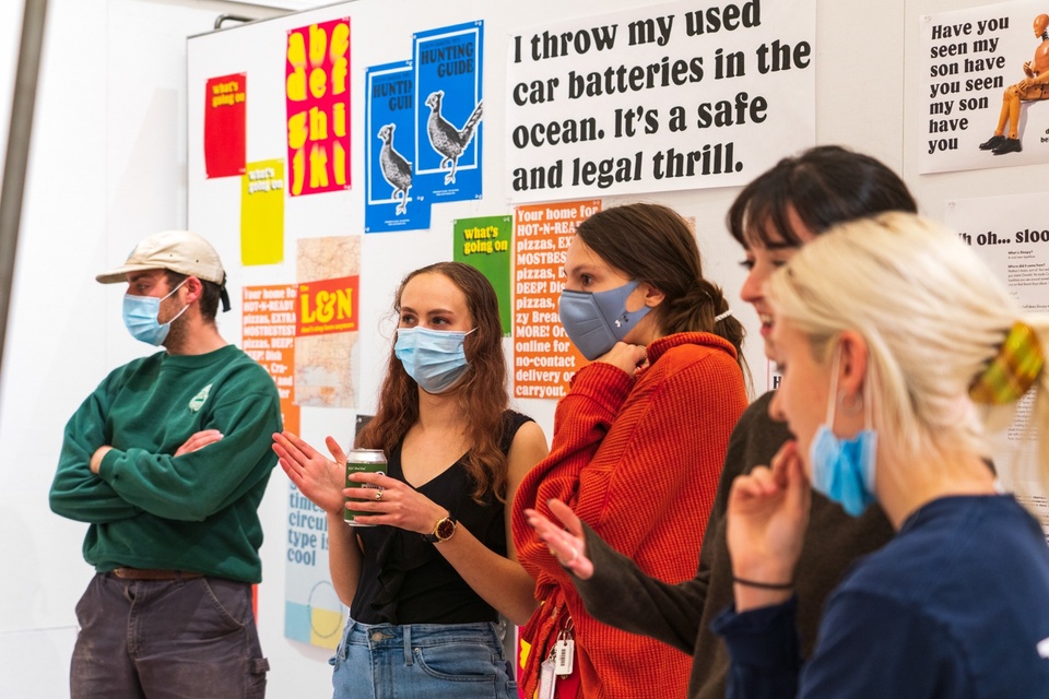 Group of students stands in front of a wall displaying type samples of a quirky rounded serif. The largest text reads "I throw my used car batteries in the ocean. It's a safe and legal thrill."