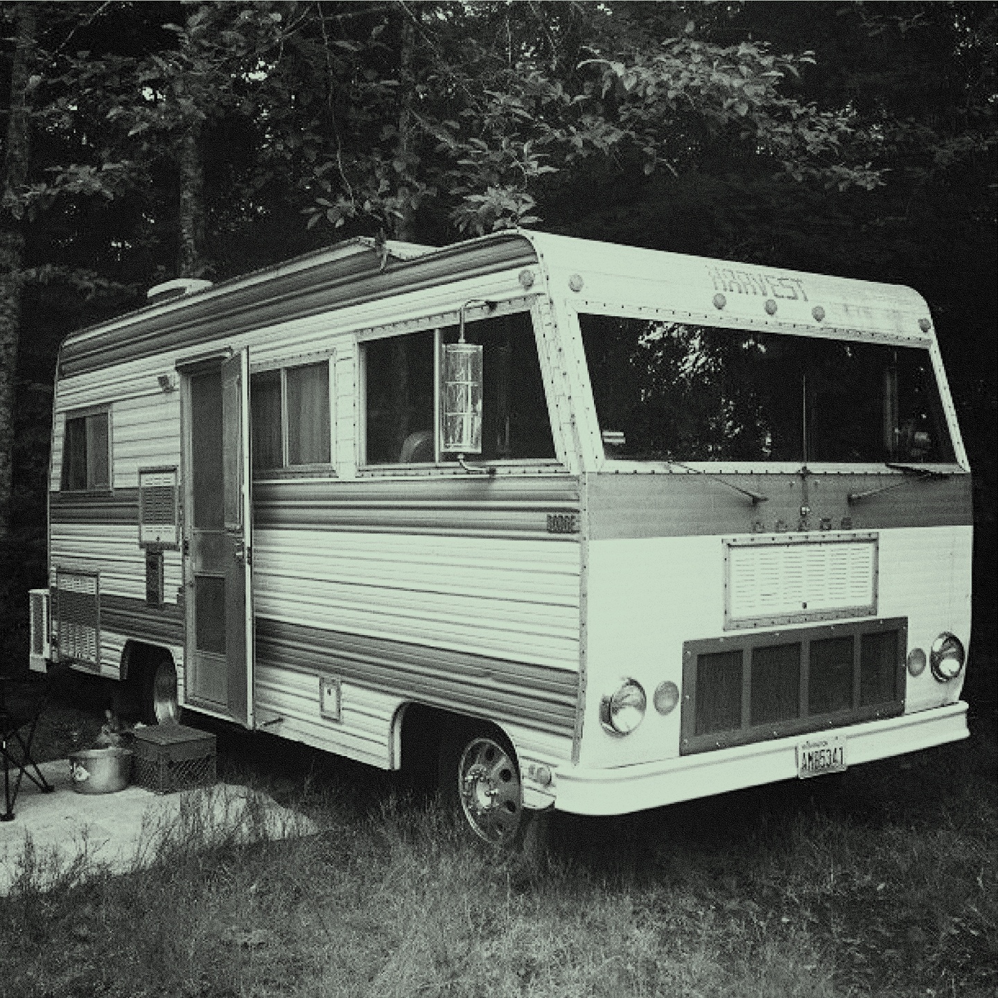 Duotone photo with a light green tint of an RV parked in a wooded area.