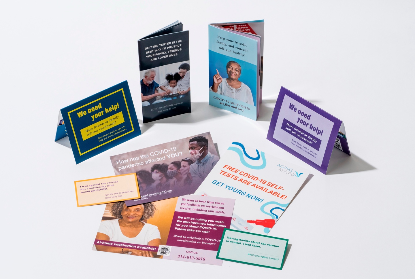 Two self-test booklets and two vaccine conversation card holders opened on a white surface. A scattering of postcards in front of them, ranging from orange and pink to blue and green.