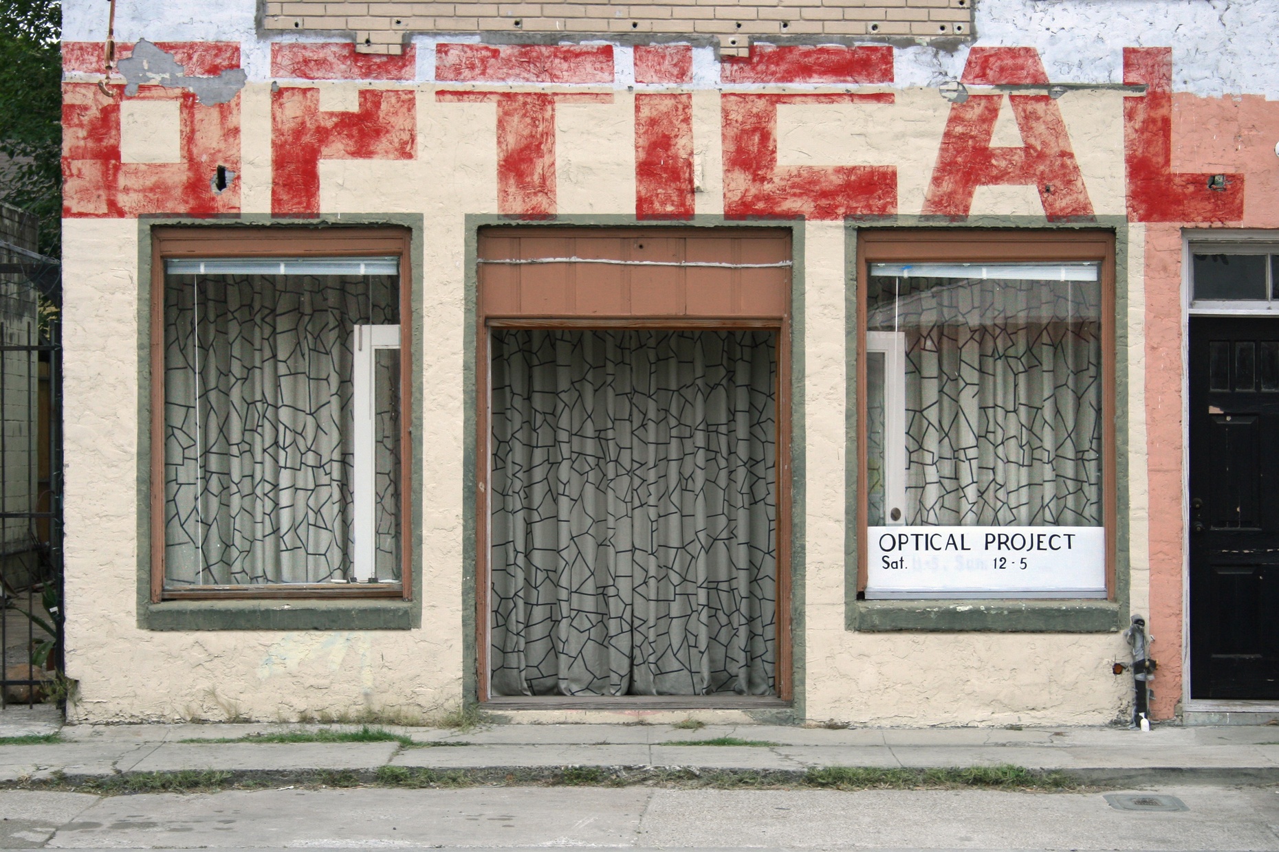 A storefront with two windows on either side of one door and the word OPTICAL written in red lettering at the top of the single story building