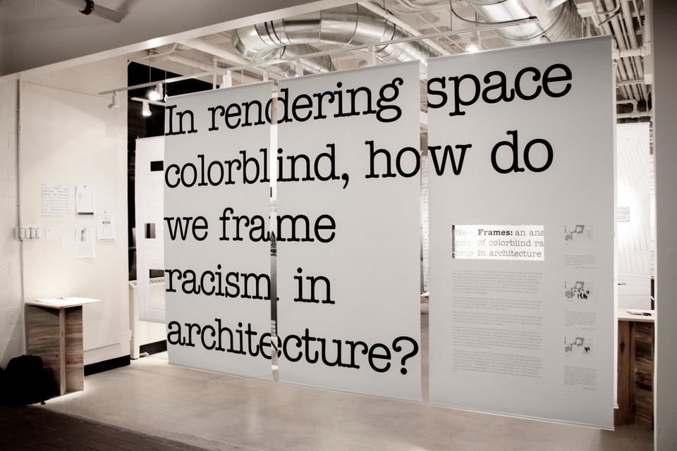 A storefront display with hanging white sheets and overlaid black text 'In rendering space colorblind, how do we frame racism in architecture?'