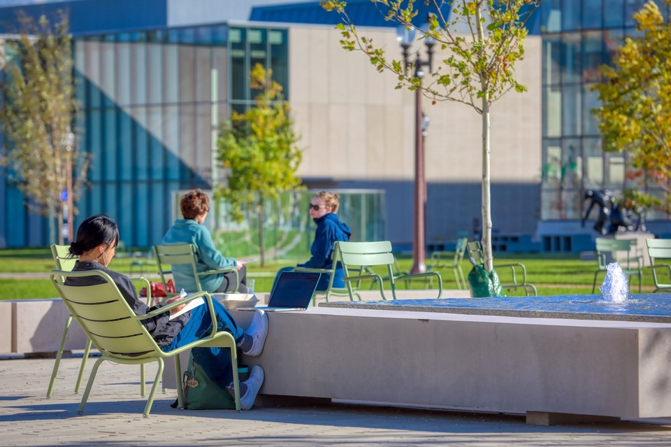 Three people relax on a brick patio with water fountains.