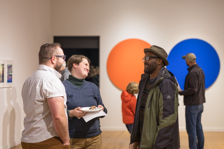 Three people smile and chat in the Des Lee Gallery.