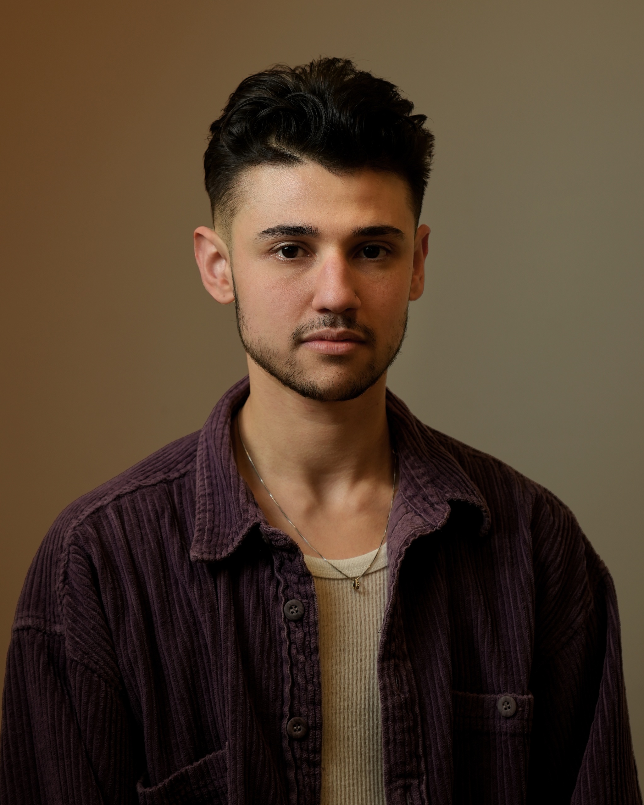 A portrait of Arzu Salman against a neutral brown background. Arzu has dark brown hair styled with a fade on the sides and a thin beard along his chin line. He looks directly at us. 