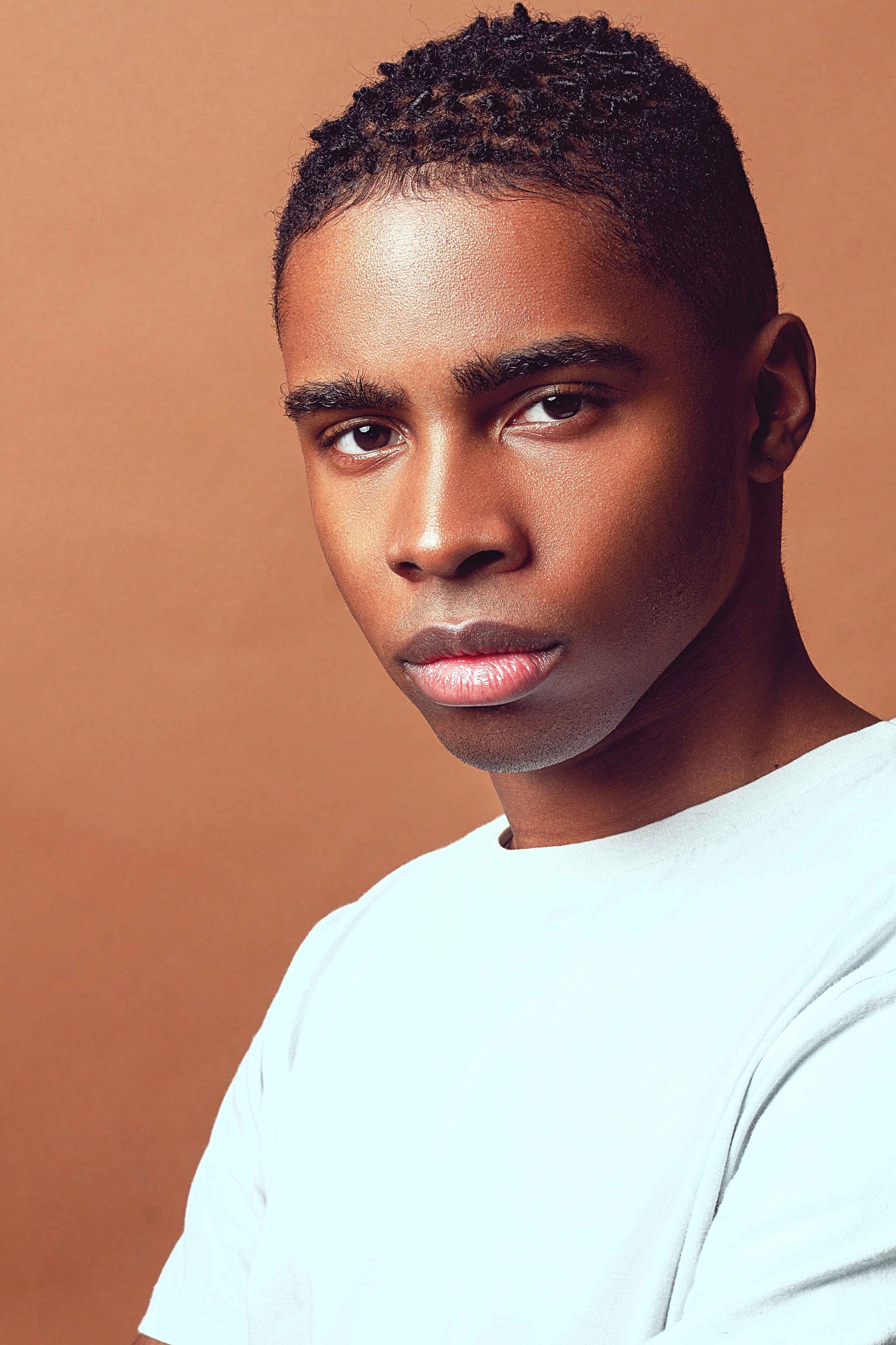 A portrait of singer Manny Dunn who looks seriously at the camera. He wears a pale blue shirt and poses against a light brown backdrop.